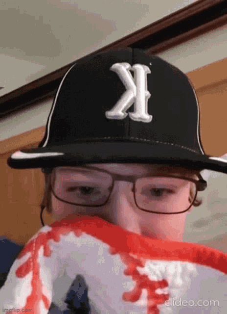 a person wearing a hat and glasses is covering their mouth with a red scarf .