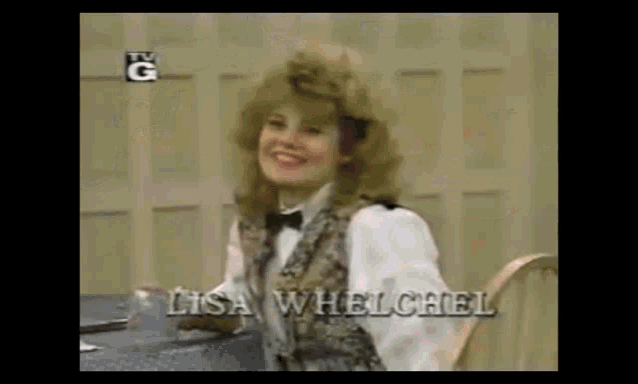 a woman in a tuxedo is sitting at a table with the name lisa wheelchel on the screen .