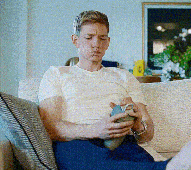 a man is sitting on a couch holding a cup and making a face