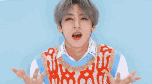 a young man wearing a blue and red vest is making a funny face with his arms outstretched .