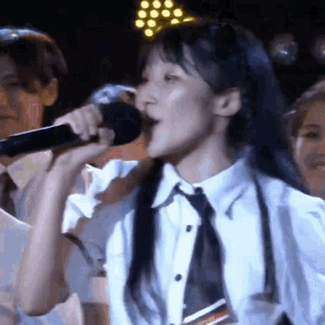 a woman is singing into a microphone while wearing a white shirt and tie .