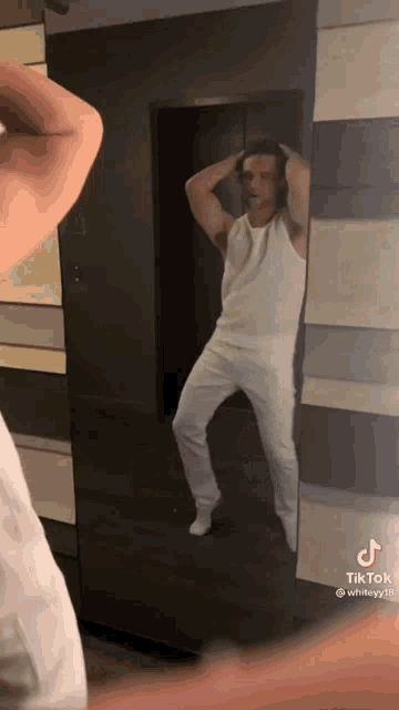 a man in white pants is standing in front of a mirror and looking at himself .