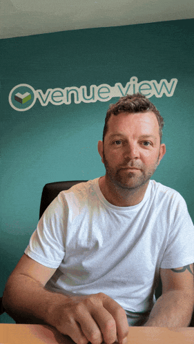 a man sits at a desk in front of a blue wall that says overview view