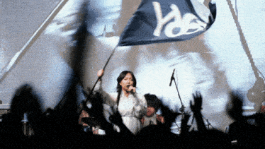 a woman singing into a microphone with a flag that says yes