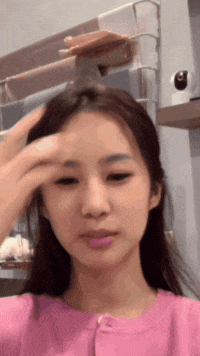 a woman in a pink shirt touches her forehead