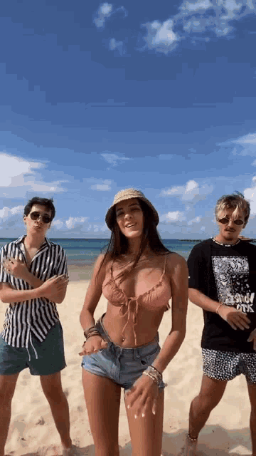 a girl in a bikini is dancing with two men on the beach