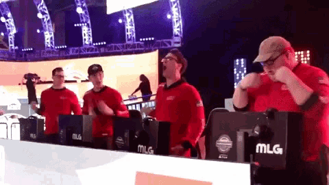 a group of men in red shirts are standing in front of monitors that say mlg on them