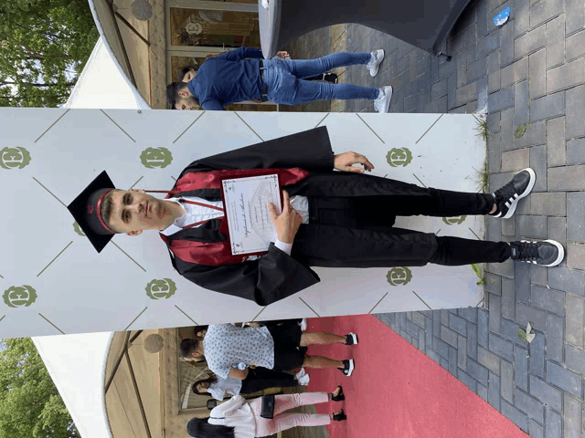 a young man in a graduation cap and gown holds a certificate