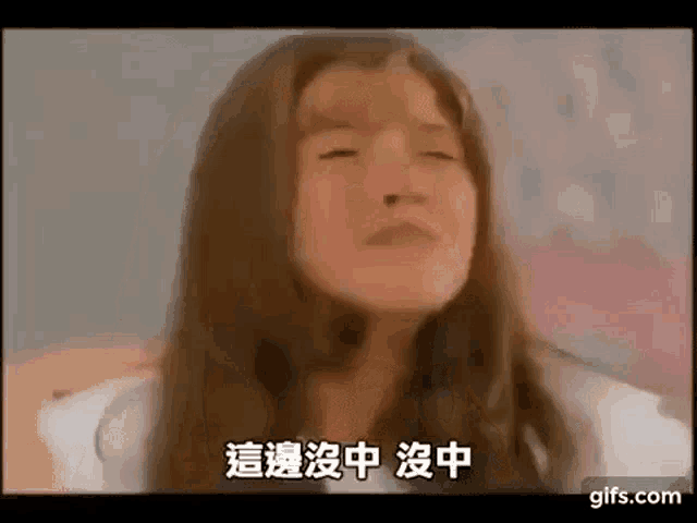 a woman with long hair is sitting on a bed with her eyes closed and chinese writing on her face .