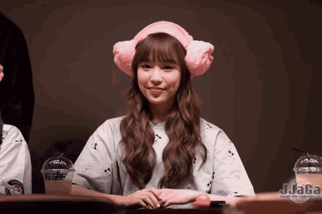 a girl wearing pink ear muffs sits at a table with a cup of jjaga