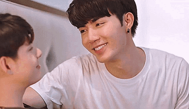 two young men are looking at each other and smiling . one of the men is wearing a white shirt .
