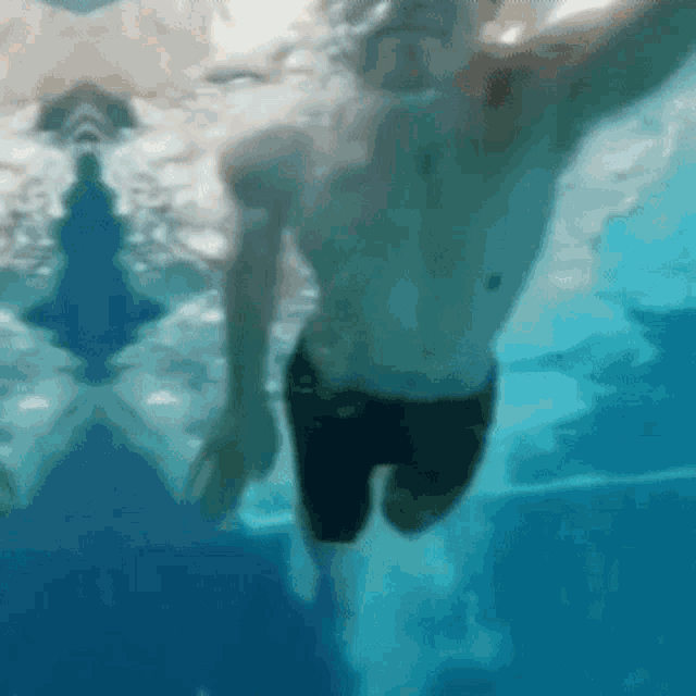 a man is swimming underwater in a pool without a shirt on .