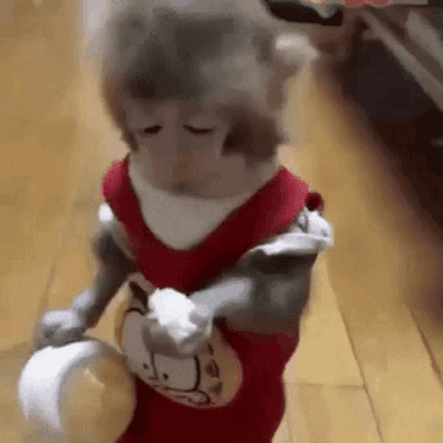 a monkey wearing a garfield shirt is standing on a wooden floor holding a bowl .