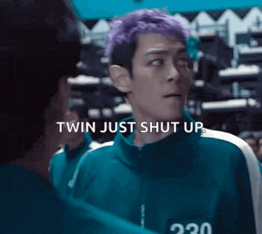 a man with purple hair is talking to another man while wearing a green jacket .