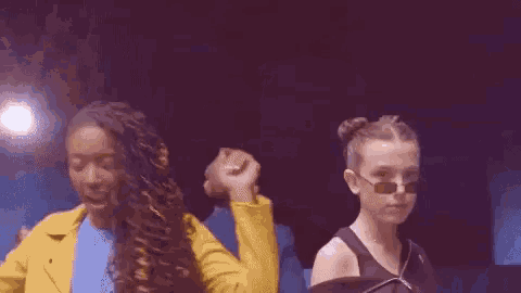 a woman wearing sunglasses is standing in a dark room with a group of people .