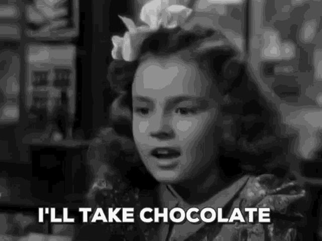 a little girl is sitting at a table with a bow in her hair and says `` i 'll take chocolate '' .