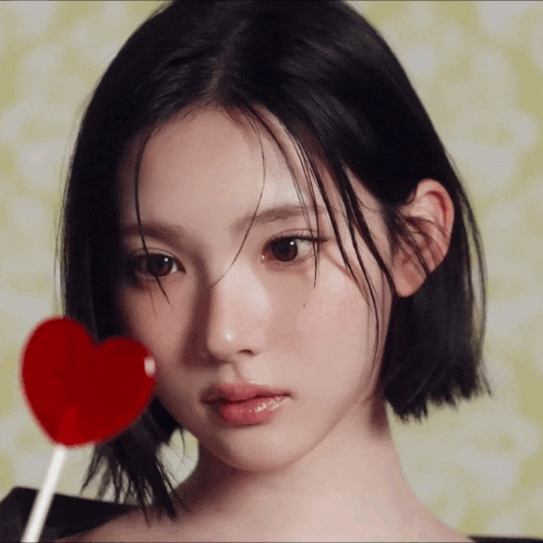 a close up of a woman holding a red heart lollipop