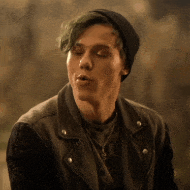 a young man with green hair is wearing a black hat and a leather jacket