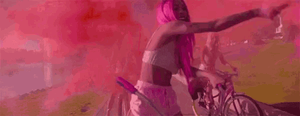 a woman with pink hair is riding a bike with pink smoke coming out of her hand .