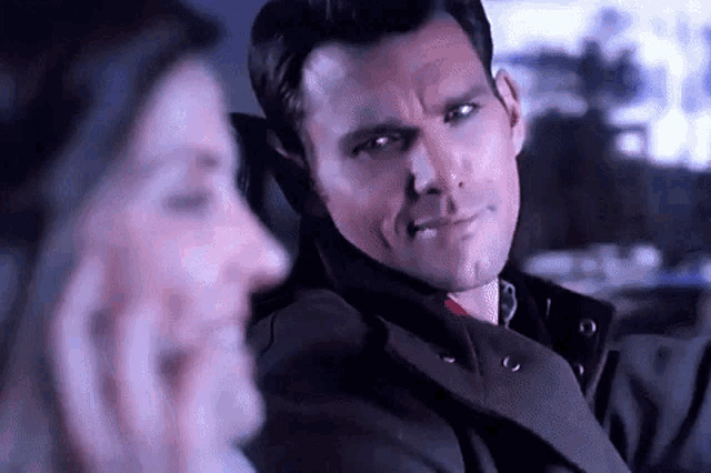 a man and a woman are sitting in a car and the man is looking at the camera .