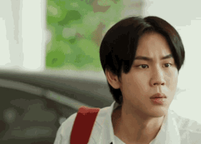 a young man wearing a white shirt and a red backpack is making a face .