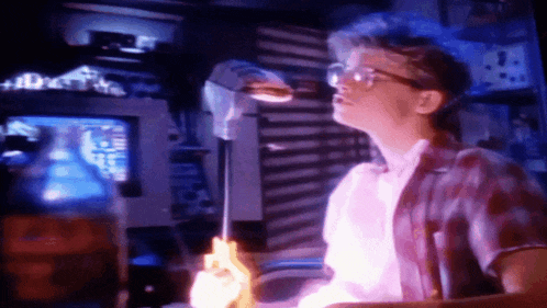 a man wearing glasses is holding a purple object in front of a computer screen
