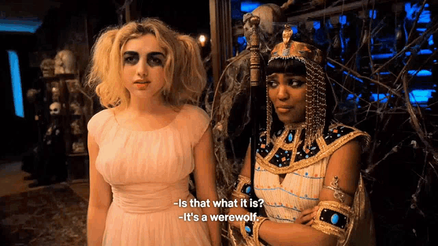 two women in costumes are standing next to each other and one of them is asking the other what it is