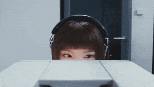 a woman wearing headphones is peeking over a desk
