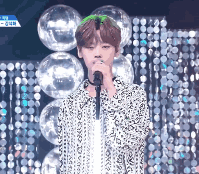 a young man singing into a microphone with a green wig on