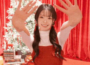 a girl in a red dress is standing in front of a christmas tree with her arms outstretched