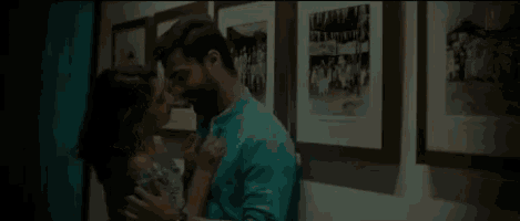 a man and a woman are kissing in front of a wall of pictures .