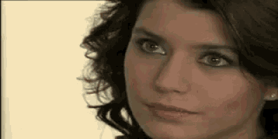 a close up of a woman 's face with curly hair and green eyes looking at the camera .