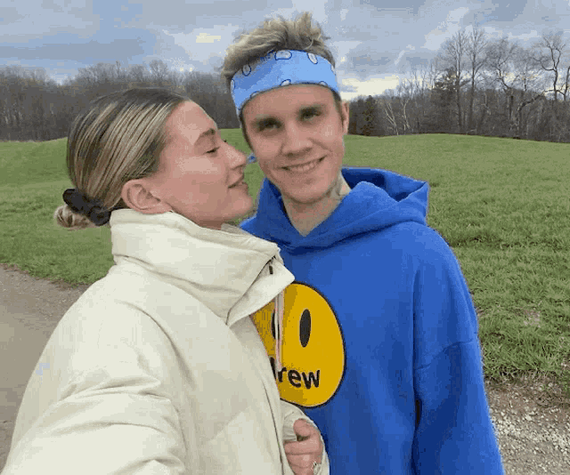 a man wearing a blue drew hoodie stands next to a woman