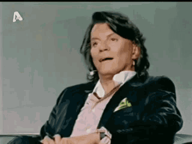 a man in a suit and pink shirt is sitting in front of a sign that says a