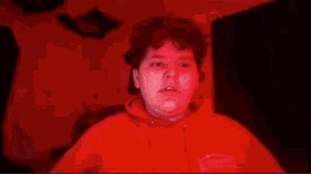 a man in a red hoodie is standing in a dark room .