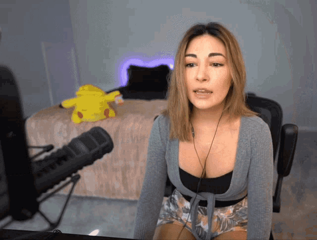 a woman is sitting in front of a microphone with a pikachu stuffed animal in the background