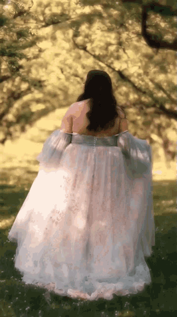 a woman in a long white dress is standing in a field .