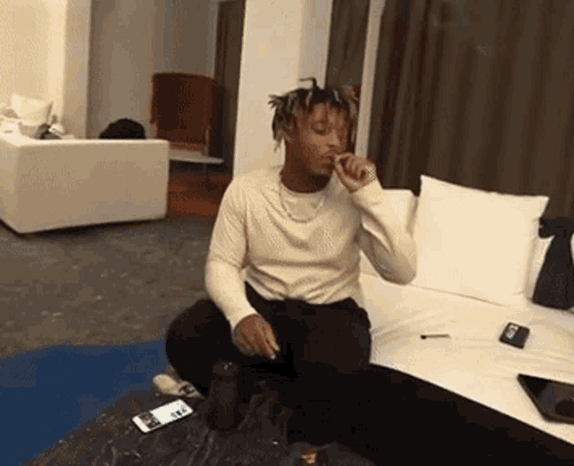 a man is smoking a cigarette while sitting on a bed in a living room .