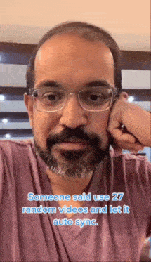 a man with glasses and a beard is sitting at a table with his head resting on his hand .