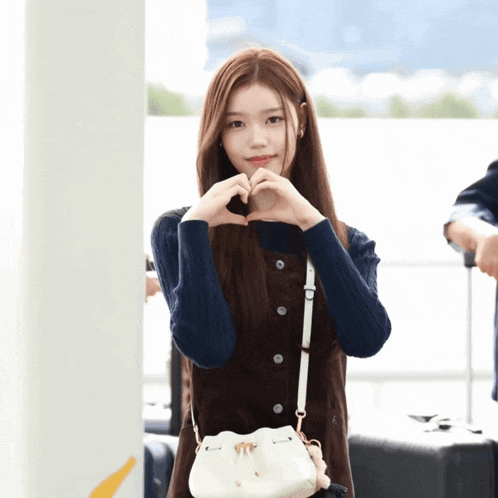 a woman making a heart shape with her hands while holding a white purse