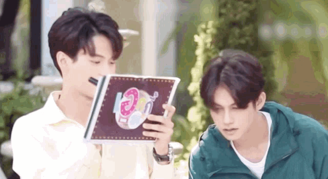 two young men are sitting next to each other and looking at a book .