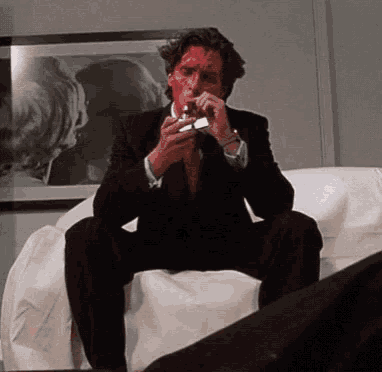 a man in a suit sitting on a couch lighting a cigarette
