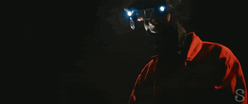 a person wearing a red jacket and a green mask is holding a knife in their hand .