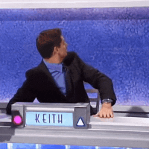 a man in a suit is sitting at a desk with a sign that says keith