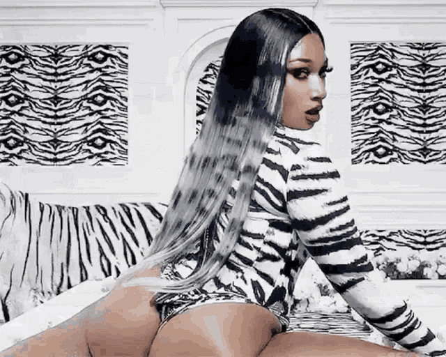 a woman in a zebra print bodysuit is sitting on a bed with a zebra print wall behind her .