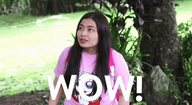 a woman in a pink shirt is standing in front of a tree with the word wow written on it .