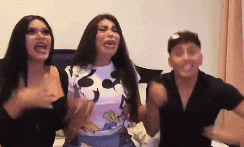 three women are standing next to each other with their mouths open and one is wearing a mickey mouse shirt .