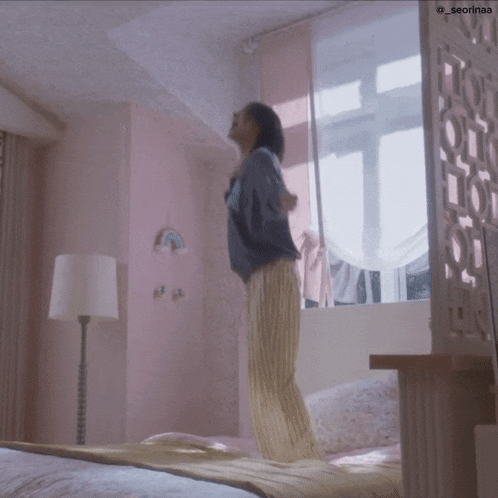 a woman in pajamas is jumping on a bed in a pink bedroom