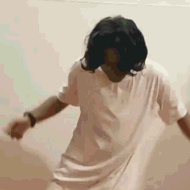 a man with long hair is dancing in front of a white wall while wearing a white shirt .