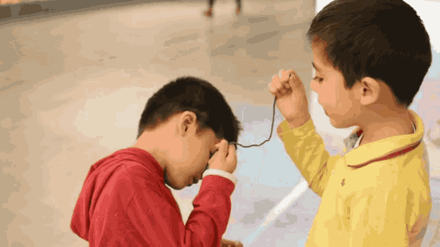 a boy in a red hoodie and a boy in a yellow shirt playing with a string